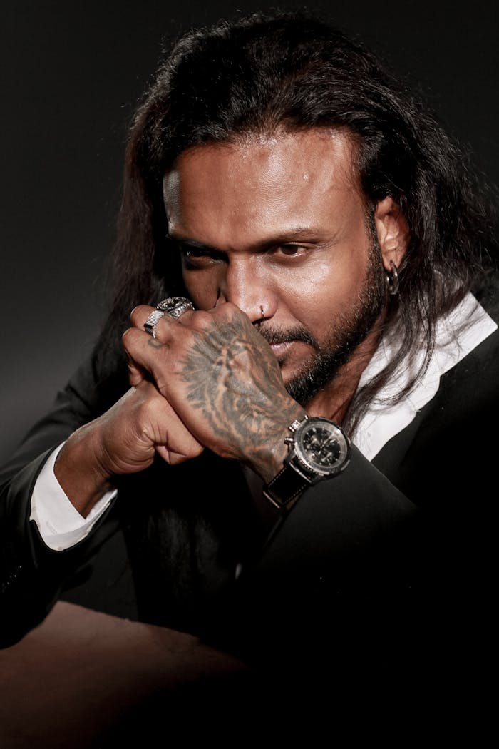 Portrait of a thoughtful man with tattooed hands, rings, and a watch, wearing a suit.